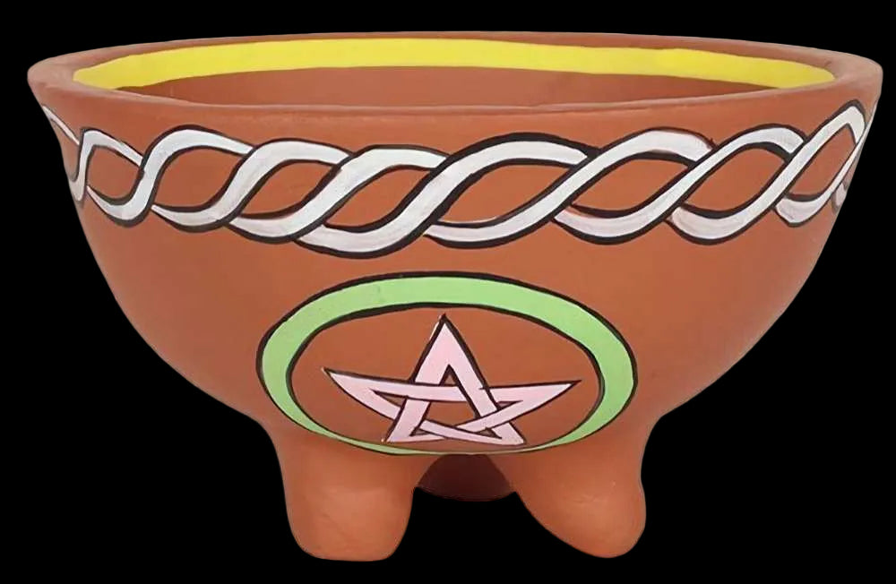 A terracotta-colored three-legged planter or bowl with hand-painted designs, including a white Celtic knot pattern on the upper half and a green circle with a pink pentagram on the front.