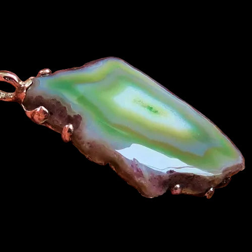 Green and brown stone pendant held by a hand on a wooden surface