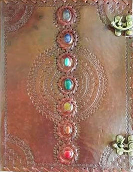 A square brown leather-bound book or journal with embossed circular mandala patterns, featuring a vertical row of colorful gemstone accents down the center and brass corner hardware.